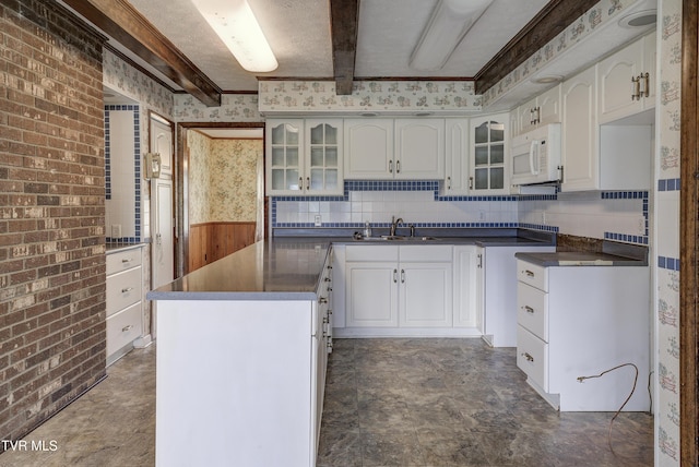 kitchen with white microwave, a sink, wainscoting, glass insert cabinets, and dark countertops
