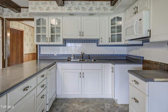 kitchen with white appliances, a sink, wallpapered walls, white cabinetry, and dark countertops