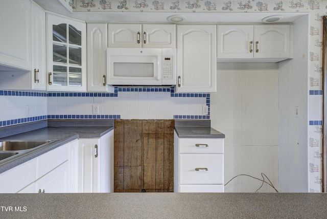 kitchen featuring white microwave, dark countertops, glass insert cabinets, and white cabinets