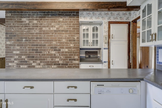 kitchen with white dishwasher, white cabinetry, glass insert cabinets, dark countertops, and wallpapered walls