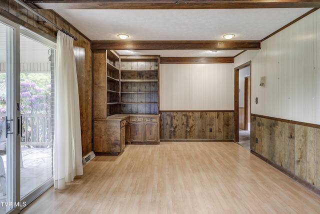 empty room featuring wooden walls, light wood-style floors, ornamental molding, and a wainscoted wall