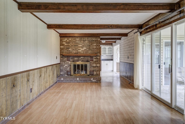 unfurnished living room featuring wood finished floors, wooden walls, beamed ceiling, and a fireplace