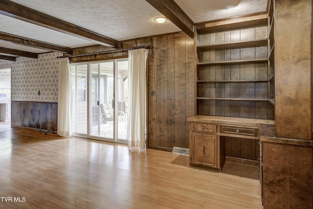 unfurnished office featuring light wood-style flooring, wood walls, beam ceiling, a textured ceiling, and wallpapered walls