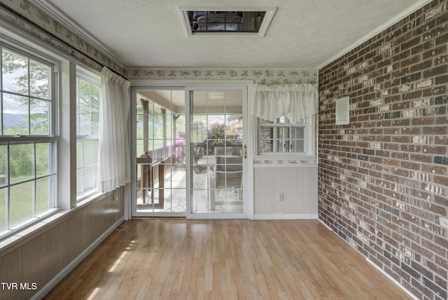 unfurnished sunroom featuring wood finished floors, a textured ceiling, brick wall, healthy amount of natural light, and baseboards