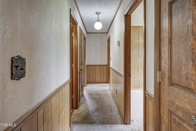 hallway with light colored carpet, ornamental molding, wainscoting, and wallpapered walls