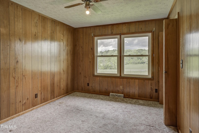 carpeted spare room with a textured ceiling, a ceiling fan, and wooden walls