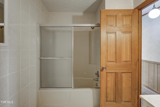 full bath with wallpapered walls, shower / bath combination with glass door, and a wainscoted wall