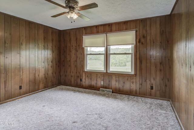 carpeted spare room featuring a ceiling fan, wooden walls, a textured ceiling, and baseboards