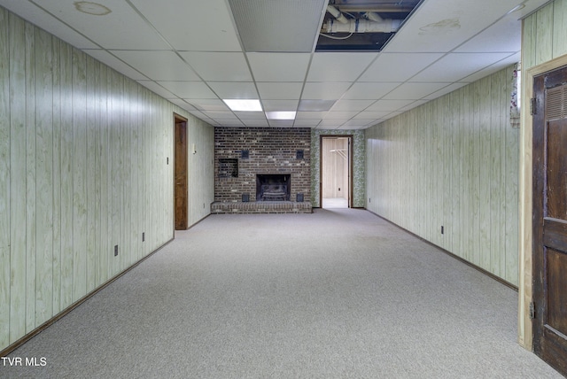 unfurnished living room featuring a fireplace, carpet flooring, a drop ceiling, and wood walls