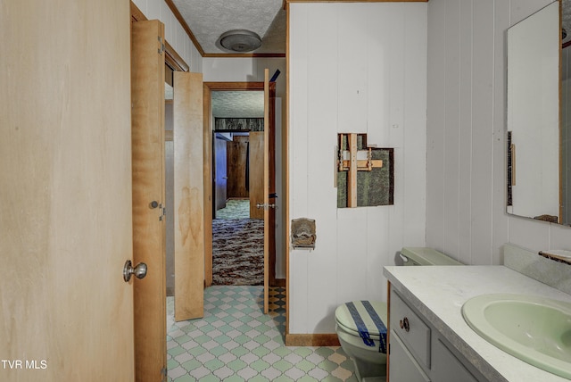 bathroom with a textured ceiling, toilet, vanity, and wood walls