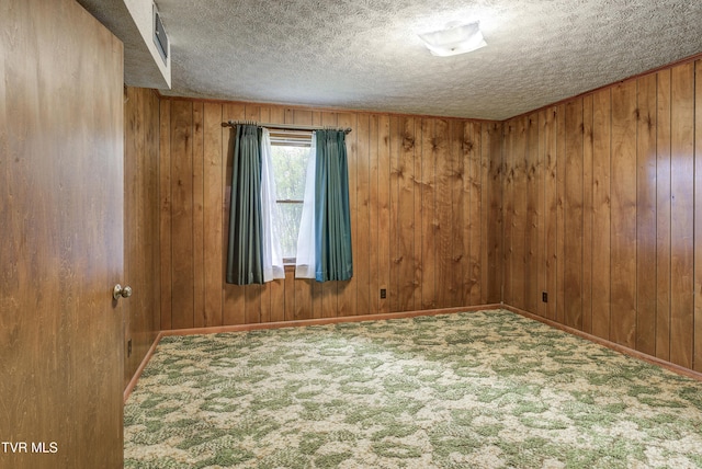 unfurnished room with carpet, a textured ceiling, wooden walls, and baseboards
