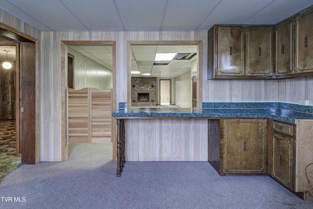 kitchen featuring carpet flooring, dark countertops, wooden walls, dark brown cabinets, and a brick fireplace