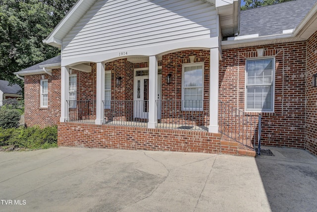 property entrance with brick siding, a porch, and roof with shingles