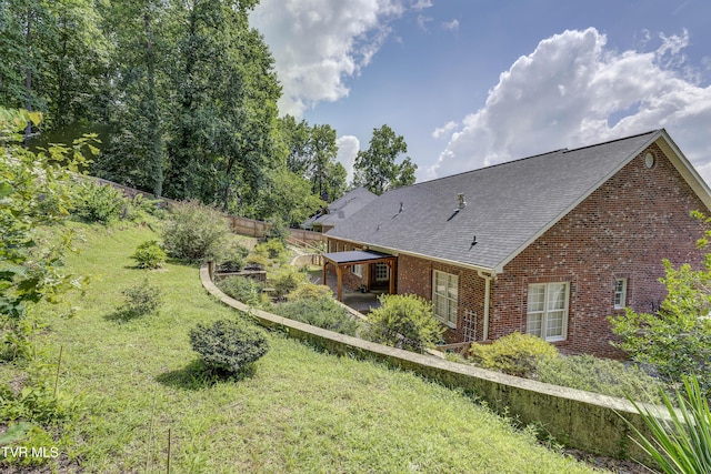 back of house featuring brick siding, a shingled roof, a yard, and a patio area