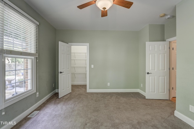 unfurnished bedroom with carpet flooring, a spacious closet, and ceiling fan
