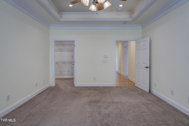 unfurnished bedroom featuring crown molding, carpet floors, a raised ceiling, and a walk in closet