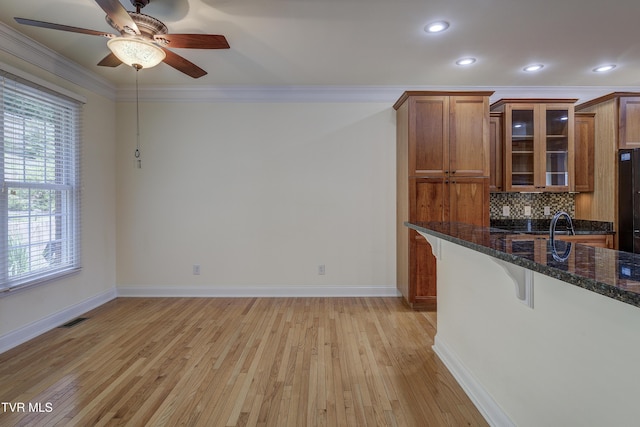 kitchen with brown cabinetry, crown molding, a breakfast bar area, light wood-style floors, and ceiling fan
