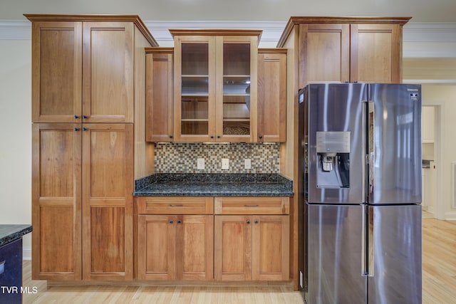 kitchen with stainless steel fridge, glass insert cabinets, dark stone counters, backsplash, and brown cabinets