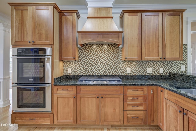 kitchen featuring stainless steel appliances, dark stone counters, tasteful backsplash, brown cabinetry, and ornamental molding