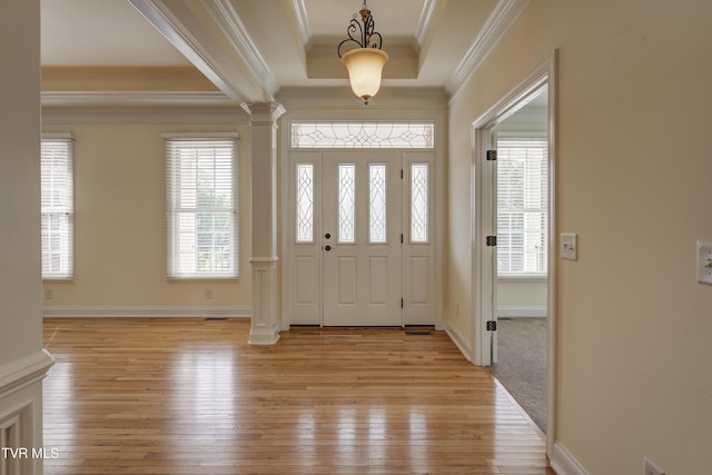 entrance foyer with ornamental molding, light wood-style floors, decorative columns, and a tray ceiling
