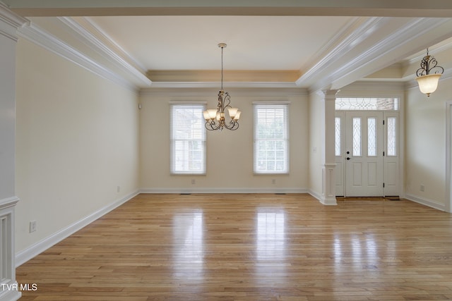 unfurnished dining area with light wood-style floors, healthy amount of natural light, a raised ceiling, ornamental molding, and a chandelier