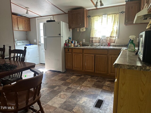 kitchen with freestanding refrigerator, a sink, dark countertops, a textured ceiling, and brown cabinetry