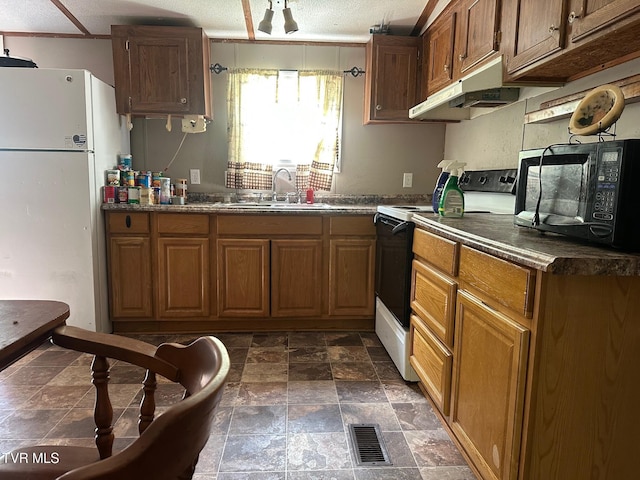 kitchen featuring white appliances, a sink, under cabinet range hood, dark countertops, and dark stone finish flooring