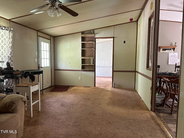 carpeted living room featuring ceiling fan and wooden walls