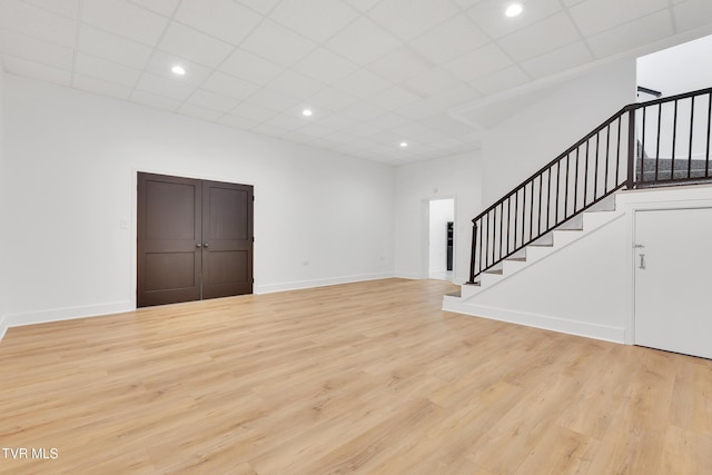 unfurnished living room featuring stairway, light wood-type flooring, baseboards, a paneled ceiling, and recessed lighting