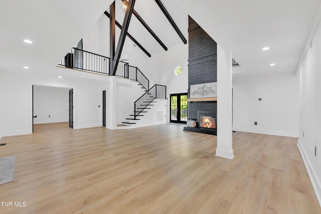 unfurnished living room with high vaulted ceiling, stairs, a brick fireplace, baseboards, and light wood-type flooring