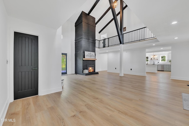 unfurnished living room with a large fireplace, light wood-type flooring, a towering ceiling, healthy amount of natural light, and baseboards