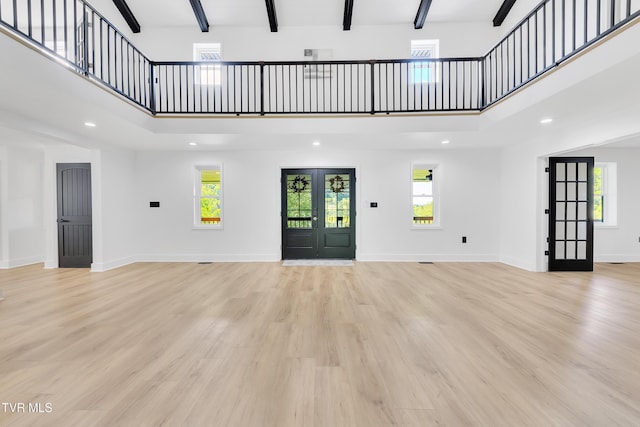 unfurnished living room featuring a towering ceiling, beamed ceiling, light wood-style flooring, baseboards, and recessed lighting