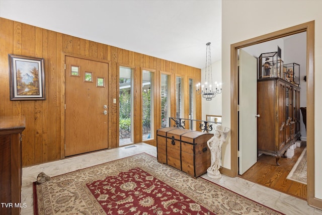 foyer featuring a chandelier, wood walls, and marble finish flooring