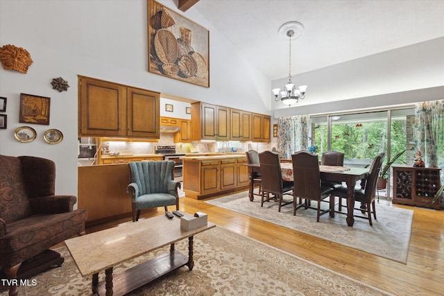dining space with high vaulted ceiling, light wood-style flooring, and a chandelier