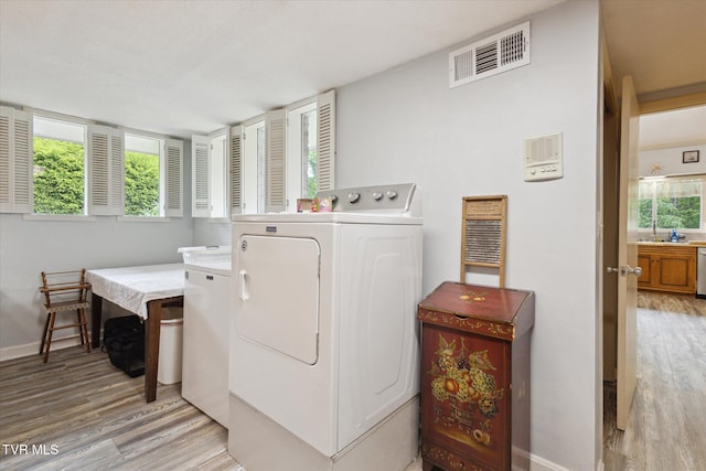 clothes washing area featuring separate washer and dryer, light wood finished floors, and baseboards