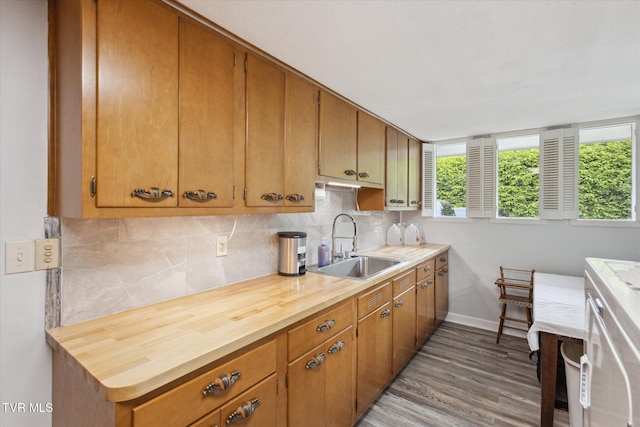 kitchen with a sink, baseboards, decorative backsplash, wood finished floors, and brown cabinetry