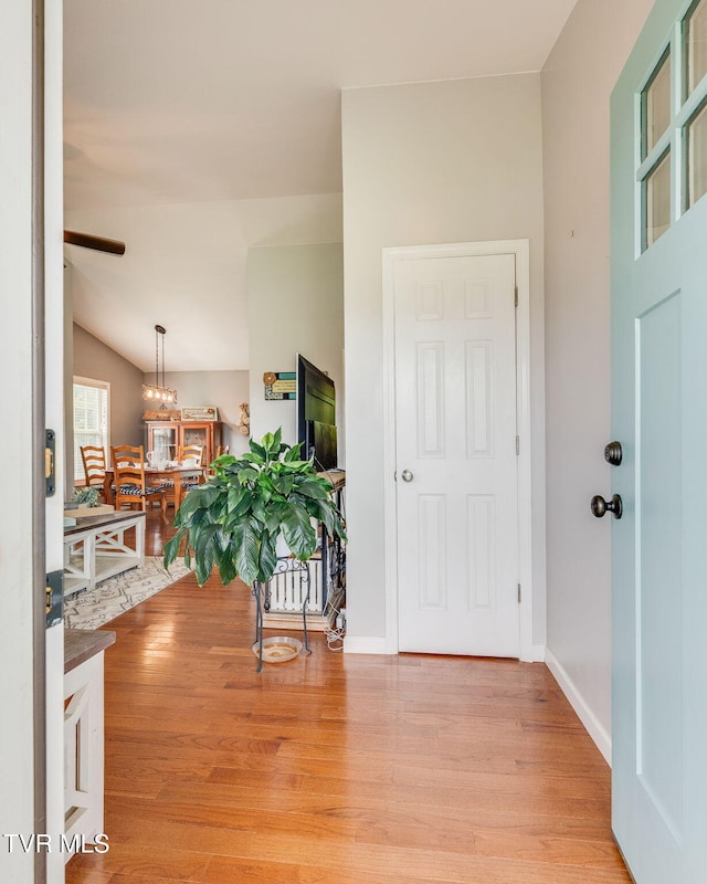 entrance foyer with light wood finished floors, ceiling fan, a chandelier, vaulted ceiling, and baseboards