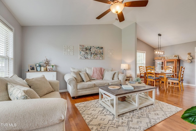 living area featuring a ceiling fan, lofted ceiling, a chandelier, light wood finished floors, and baseboards