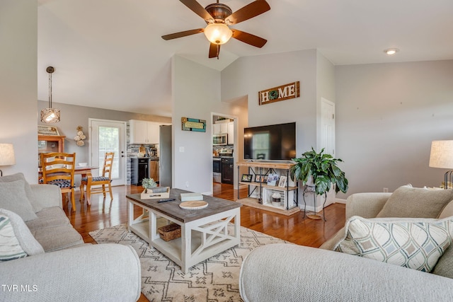 living area featuring light wood-style floors, ceiling fan, vaulted ceiling, and baseboards