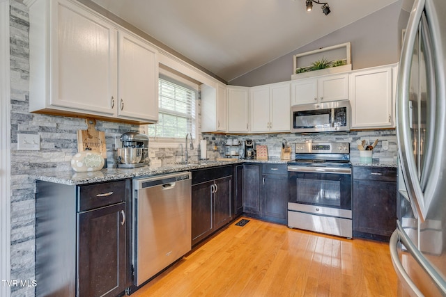 kitchen featuring stainless steel appliances, vaulted ceiling, a sink, white cabinets, and light wood finished floors