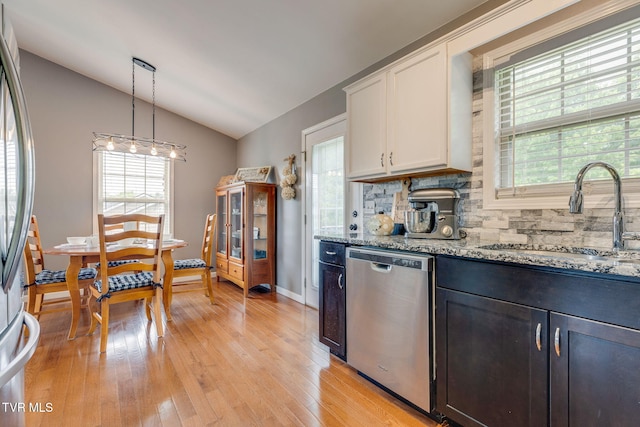 kitchen with appliances with stainless steel finishes, a sink, vaulted ceiling, light stone counters, and decorative backsplash