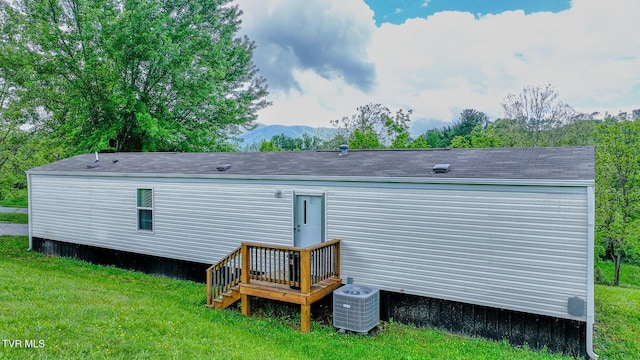 rear view of property with cooling unit, a lawn, a mountain view, and roof with shingles