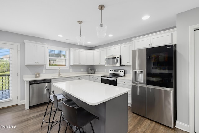kitchen with stainless steel appliances, a sink, white cabinetry, light countertops, and a kitchen island