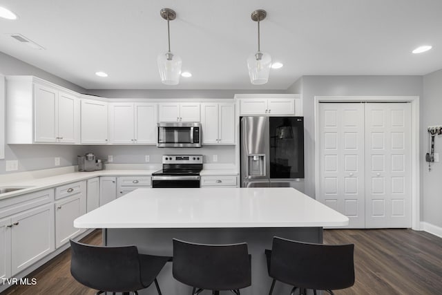 kitchen featuring appliances with stainless steel finishes, a kitchen bar, white cabinetry, a kitchen island, and dark wood-style floors