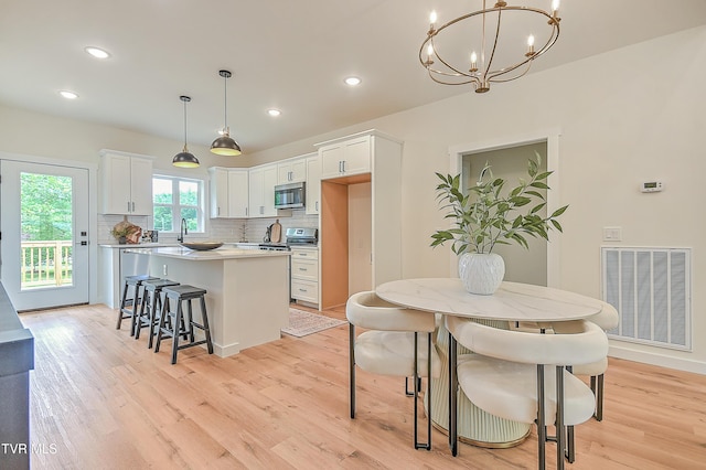 kitchen with stainless steel appliances, a center island, a chandelier, tasteful backsplash, and light wood-style flooring