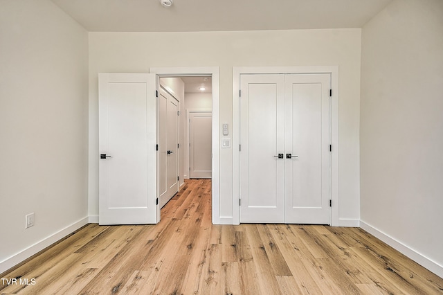 unfurnished bedroom featuring light wood-style flooring, baseboards, and a closet