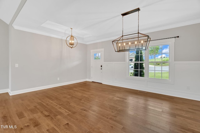 unfurnished dining area featuring a chandelier, crown molding, wood finished floors, a wainscoted wall, and a tray ceiling