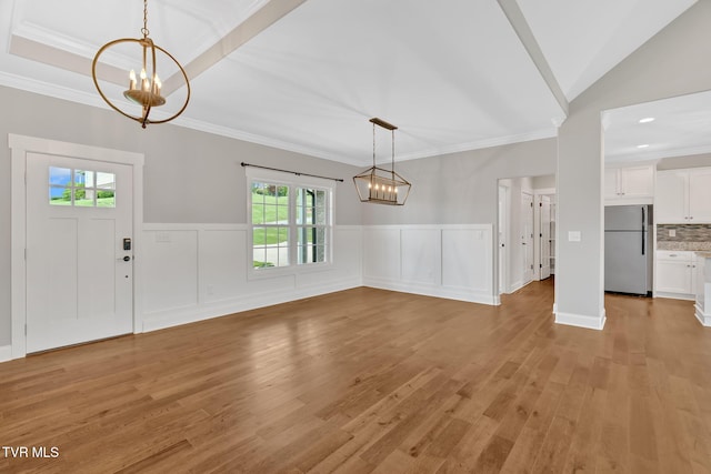 foyer entrance with a chandelier, light wood finished floors, ornamental molding, and a wainscoted wall