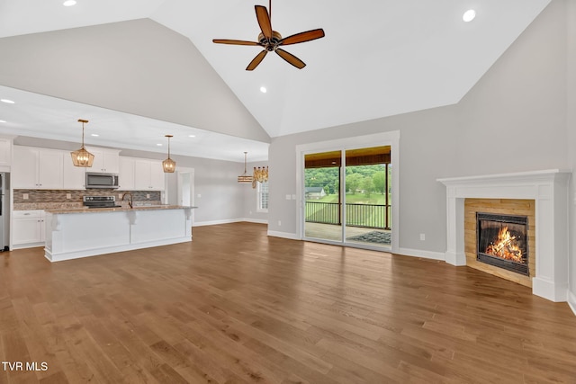 unfurnished living room featuring high vaulted ceiling, a fireplace, ceiling fan, recessed lighting, and a sink