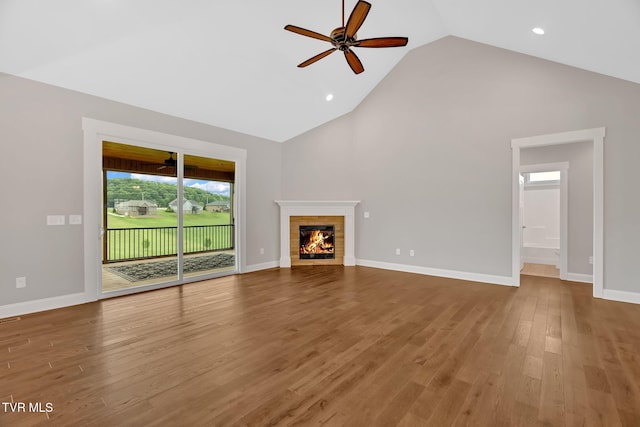 unfurnished living room featuring ceiling fan, wood finished floors, high vaulted ceiling, a brick fireplace, and baseboards